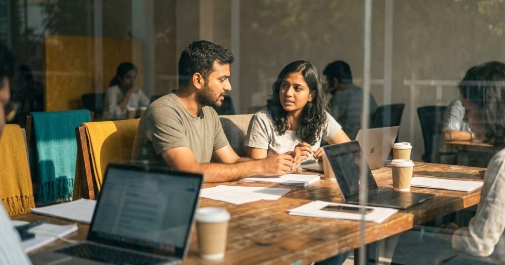 Two Indian founders discuss strategies in a coworking space, echoing low-budget marketing and customer acquisition techniques.