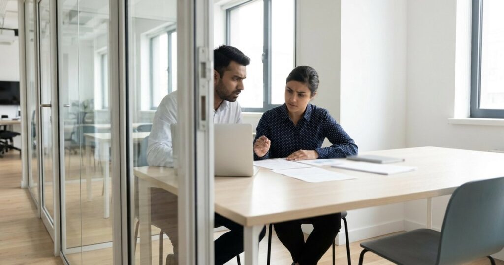 Two professionals discuss FC-GPR filing in an office, surrounded by papers and a laptop with blurred text.